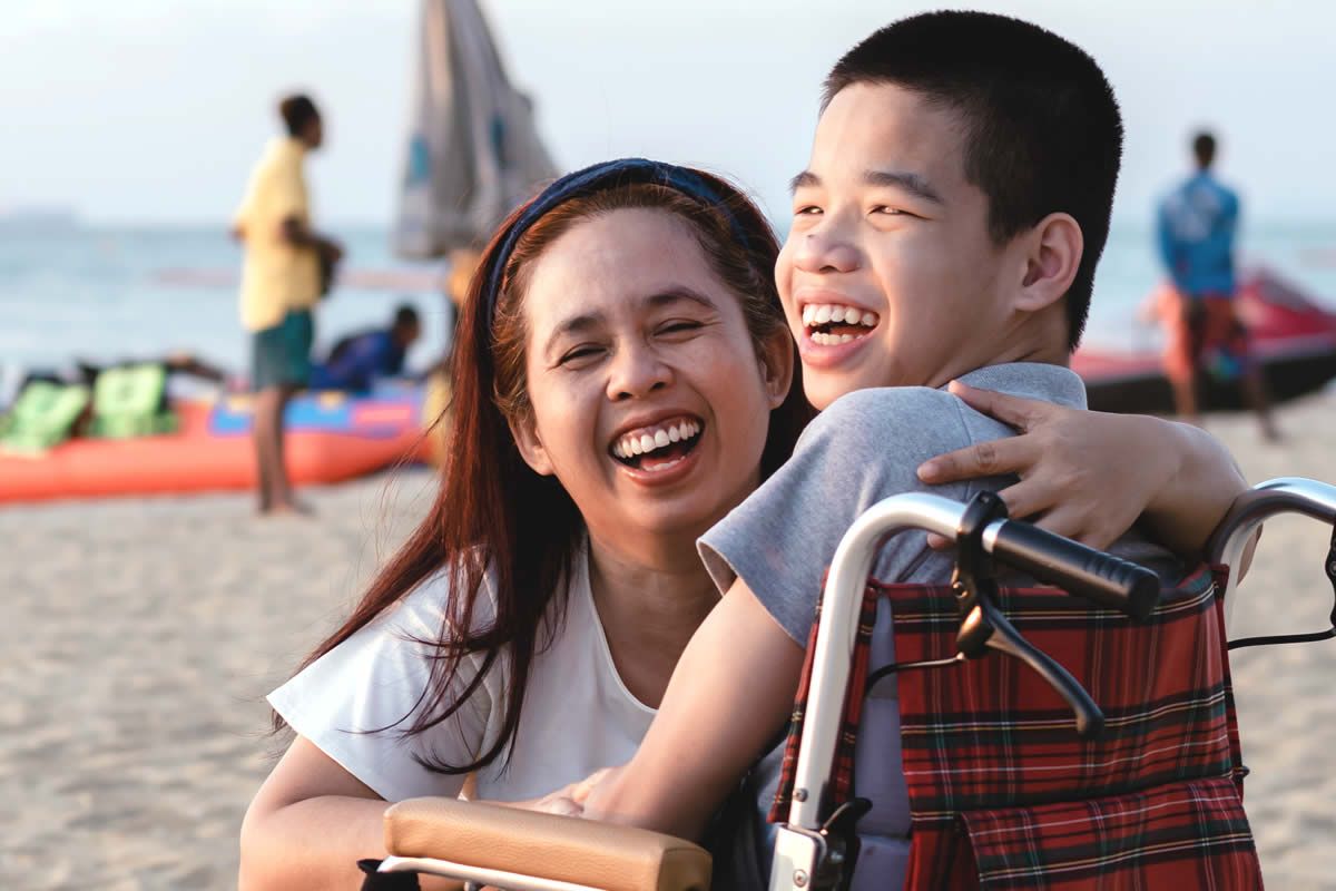 Woman smiling with teen boy in wheelchair at the beach