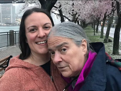 A white woman and her mother. In the background are blooming trees.