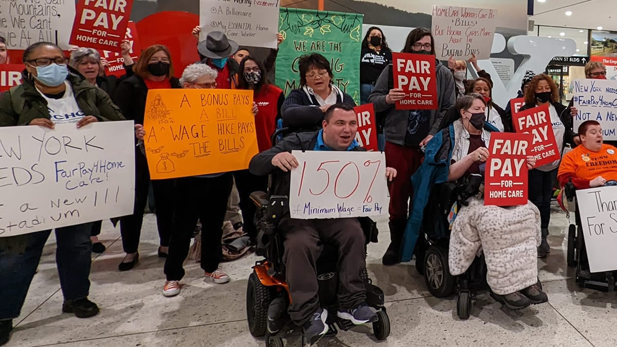 Large group of people holding signs for increase in minimum wage and home care advocacy